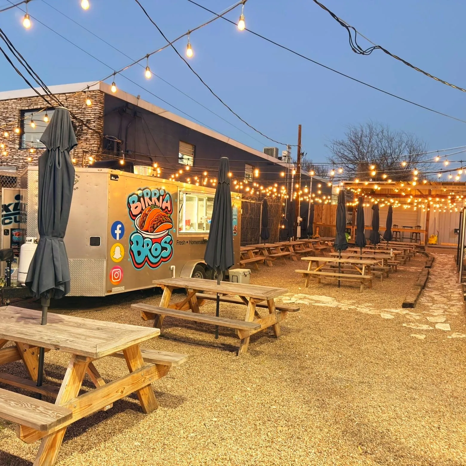 Birria Bros trailer parked at a food-truck park with string lights at dusk